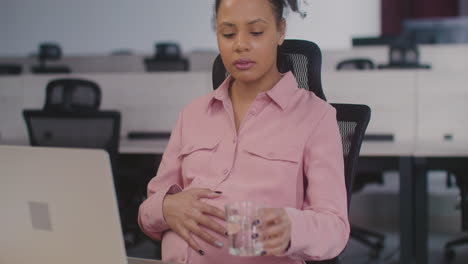 Schwangere-Frau,-Die-Ihren-Bauch-Streichelt-Und-Wasser-Trinkt,-Während-Sie-Im-Büro-Arbeitet-1