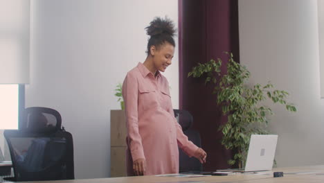 Happy-Pregnant-Woman-Dancing-While-Standing-At-Desk-In-The-Office