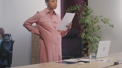 Pregnant-Woman-Checking-Documents-And-Drinking-Water-While-Standing-At-Desk-In-The-Office-1