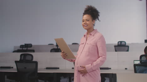 Portrait-Of-A-Beautiful-Pregnant-Woman-Holding-Documents-And-Smiling-At-Camera-While-Working-In-The-Office