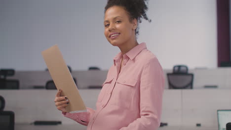 Portrait-Of-A-Smiling-Pregnant-Woman-Caressing-Her-Belly-And-Smiling-At-Camera-In-The-Office-1