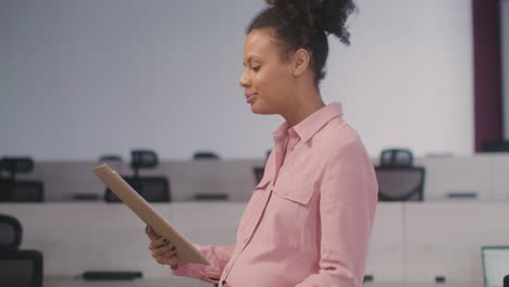 Portrait-Of-A-Smiling-Pregnant-Woman-Holding-Documents-And-Smiling-At-Camera-In-The-Office