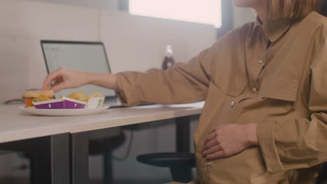 Close-Up-Of-Working-Pregnant-Woman-Eating-Nuggets-During-Office-Lunch-Break