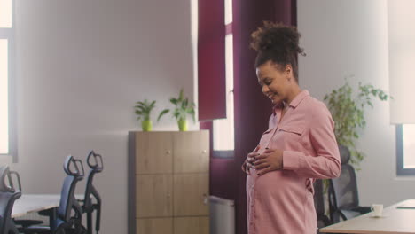 Pregnant-Happy-Woman-Posing-At-Camera-While-Touching-Her-Belly-In-The-Office-1