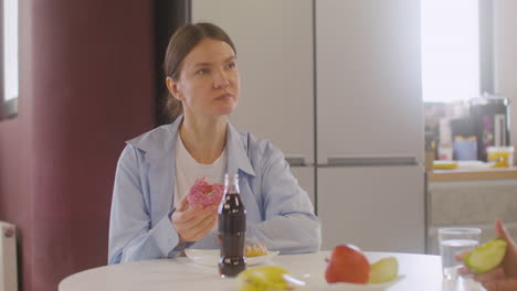 Pregnant-Woman-Sitting-At-Table-Eating-A-Donut-And-Talking-With-Coworker-In-Canteen