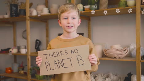 Blond-Kid-In-Craft-Workshop-Holding-A-Cardboard-Sign-With-There's-No-Planet-B-Phrase