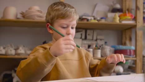 Blond-Kid-Drawing-Sitting-At-A-Table-In-A-Craft-Workshop-1