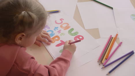 Top-View-Of-Blonde-Little-Girl-Drawing-The-Phrase-Save-The-Earth-On-A-Paper-On-A-Table-In-Craft-Workshop-1