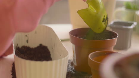 Close-Up-View-Of-Unrecognizable-Girl-Preparing-The-Soil-In-A-Pot-Sitting-At-A-Table-Where-Is-Plants-In-A-Craft-Workshop