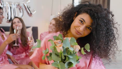 Muslimische-Frau,-Die-Einen-Blumenstrauß-Hält-Und-Riecht,-Rosa-Seidennachthemd-Trägt,-Lächelt-Und-In-Die-Kamera-Schaut