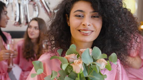 Nahaufnahme-Einer-Muslimischen-Frau,-Die-Einen-Blumenstrauß-Hält-Und-Ein-Rosafarbenes-Nachthemd-Aus-Seide-Trägt,-Das-Lächelt-Und-In-Die-Kamera-Blickt