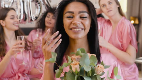 Woman-Holding-Bouquet,-Wearing-Pink-Silk-Nightdress,-Smiling-While-Touching-Her-Hair-And-Looking-At-Camera