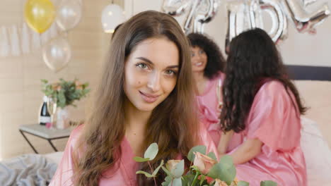 Brunette-Woman-Holding-And-Smelling-A-Bouquet,-Wearing-Pink-Silk-Nightdress,-Smiling-And-Looking-At-Camera