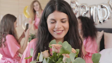 Brunette-Woman-Holding-And-Smelling-A-Bouquet,-Wearing-Pink-Silk-Nightdress,-Smiling-And-Looking-At-Camera-1