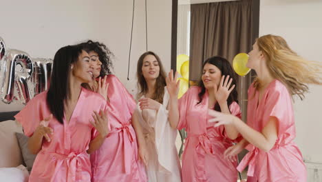 Gruppe-Multiethnischer-Freundinnen-Und-Braut,-Die-Rosafarbene-Und-Weiße-Seidennachthemden-Tragen,-Während-Sie-In-Einem-Raum-In-Der-Brautversammlung-Tanzen-1