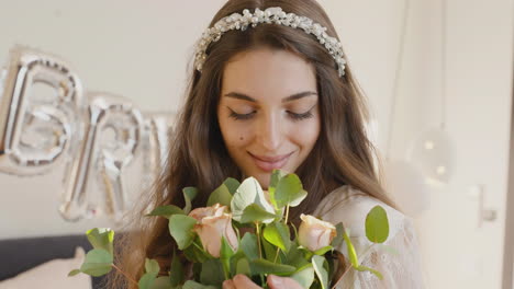Bride-Holding-And-Smelling-Bouquet-With-Hair-Band-With-Flowers,-Looking-At-Camera-While-Smiling