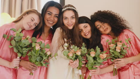 Group-Of-Multiethnic-Female-Friends-And-Bride-Looking-At-Camera,-Wearing-Silk-Pink-And-White-Nighdresses-While-Holding-Bouquets-2