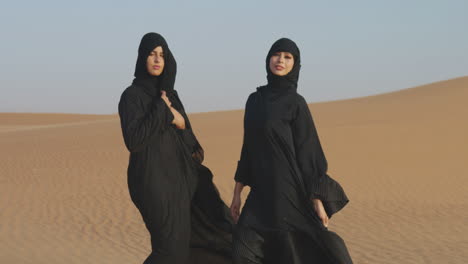 Zwei-Schöne-Muslimische-Frauen-Im-Hijab-Posieren-In-Einer-Windigen-Wüste-Und-Blicken-In-Die-Kamera-1