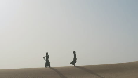 Extreme-Long-Shot-Of-Two-Muslim-Women-Wearing-Traditional-Black-Dress-And-Hijab-Walking-In-A-Windy-Desert-1