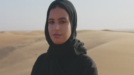 Porträt-Einer-Schönen-Muslimischen-Frau-Mit-Hijab,-Die-In-Einer-Windigen-Wüste-In-Die-Kamera-Blickt-1