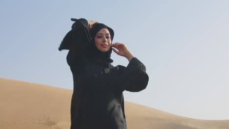 Hermosa-Mujer-Musulmana-Con-Vestido-Negro-Tradicional-Y-Hiyab-Posando-En-Un-Desierto-Ventoso