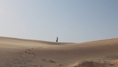 Extreme-Long-Shot-Of-A-Muslim-Woman-In-Traditional-Dress-And-Hijab-Walking-In-A-Windy-Desert