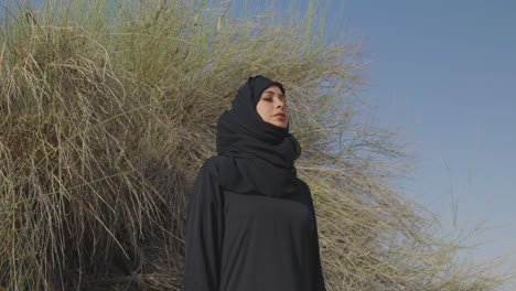 Porträt-Einer-Schönen-Muslimischen-Frau-In-Traditioneller-Kleidung-Und-Hijab,-Die-Mit-Geschlossenen-Augen-In-Der-Nähe-Eines-Wüstenstrauchs-Steht