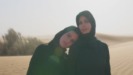 Porträt-Von-Zwei-Muslimischen-Frauen-In-Hijab,-Die-In-Einer-Windigen-Wüste-Stehen