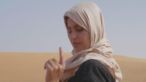 Muslimische-Frau-Im-Hijab,-Die-Ihre-Hand-Sanft-In-Einer-Windigen-Wüste-Bewegt