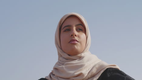 Porträt-Einer-Muslimischen-Frau-Im-Hijab,-Die-In-Einer-Windigen-Wüste-Tanzt-Und-Ihre-Hände-Sanft-Bewegt