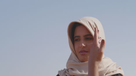 Porträt-Einer-Muslimischen-Frau-Im-Hijab,-Die-In-Einer-Windigen-Wüste-Tanzt-Und-Ihre-Hände-Sanft-Bewegt-1