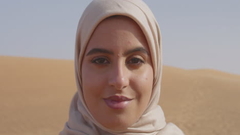 Nahaufnahme-Des-Porträts-Einer-Schönen-Muslimischen-Frau-Im-Hijab,-Die-In-Einer-Windigen-Wüste-Steht-Und-In-Die-Kamera-Blickt-1