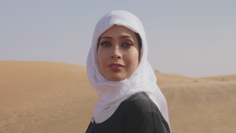 Porträt-Einer-Schönen-Muslimischen-Frau-In-Weißem-Hijab-Und-Traditionellem-Schwarzem-Kleid,-Die-In-Einer-Windigen-Wüste-Steht-Und-In-Die-Kamera-Lächelt-1
