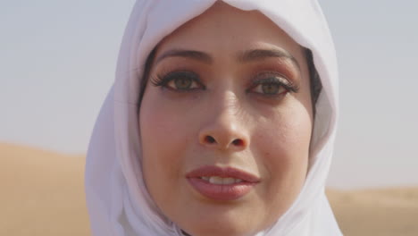 Nahaufnahme-Porträt-Einer-Schönen-Muslimischen-Frau-In-Weißem-Hijab,-Die-In-Einer-Windigen-Wüste-Steht-Und-In-Die-Kamera-Lächelt