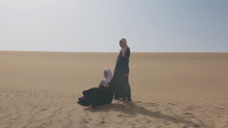 Two-Muslim-Women-Wearing-Traditional-Dress-And-Hijab-Posing-In-A-Windy-Desert