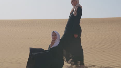 Zwei-Muslimische-Frauen-In-Traditioneller-Kleidung-Und-Hijab-Posieren-In-Einer-Windigen-Wüste-1