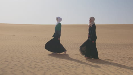 Dos-Mujeres-Musulmanas-Con-Vestido-Tradicional-Y-Hiyab-Caminando-Juntas-En-Un-Desierto-Ventoso