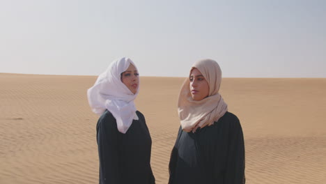 Two-Muslim-Women-Wearing-Traditional-Dress-And-Hijab-Standing-In-A-Windy-Desert