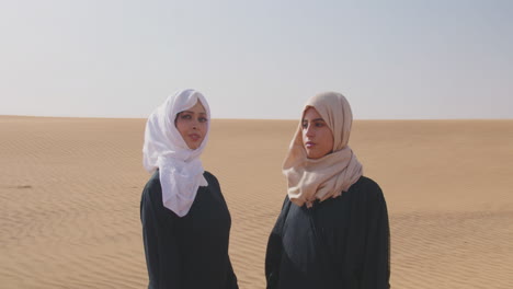 Two-Muslim-Women-Wearing-Traditional-Dress-And-Hijab-Standing-In-A-Windy-Desert-1