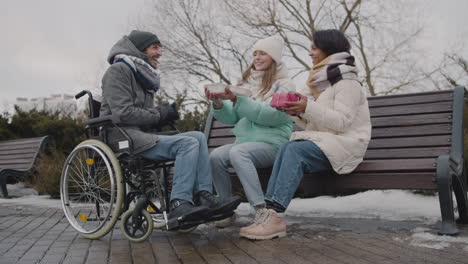 Happy-Disabled-Man-In-Wheelchair-Celebrating-His-Birthday-With-Two-Friends-At-Urban-Park-In-Winter