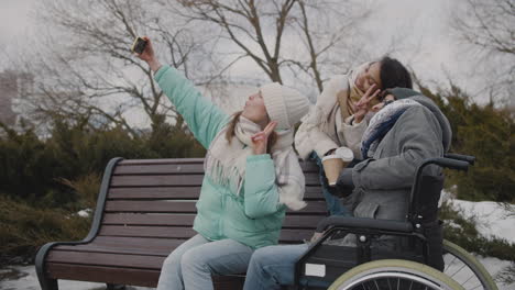 Gruppe-Von-Freunden,-Zwei-Frauen-Und-Ein-Behinderter-Mann-Im-Rollstuhl,-Die-Während-Der-Wintersaison-1-Ein-Selfie-Video-Im-Stadtpark-Machen