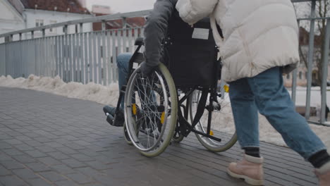 Persona-Discapacitada-En-Silla-De-Ruedas-Dando-Un-Paseo-Con-Su-Amigo-Por-La-Ciudad-En-Invierno