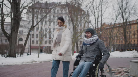Muslimische-Frau-Und-Ihre-Behinderte-Freundin-Im-Rollstuhl-Gehen-Im-Winter-In-Der-Stadt-Spazieren