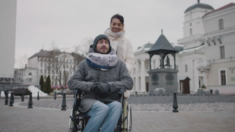 Muslimische-Frau,-Die-Im-Winter-1-Ihren-Behinderten-Freund-Im-Rollstuhl-Auf-Einem-Spaziergang-Durch-Die-Stadt-Mitnimmt