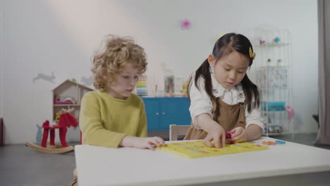 Kleines-Mädchen-Und-Kleiner-Junge-Spielen-Mit-Alphabet-Puzzle-In-Der-Montessori-Schule,-Während-Andere-Schüler-Im-Klassenzimmer-Laufen