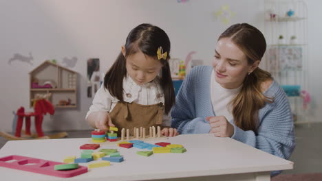 Little-Girl-In-A-Montessori-School-Playing-With-Shapes-Stacking-While-Teacher-Helping-Her-1