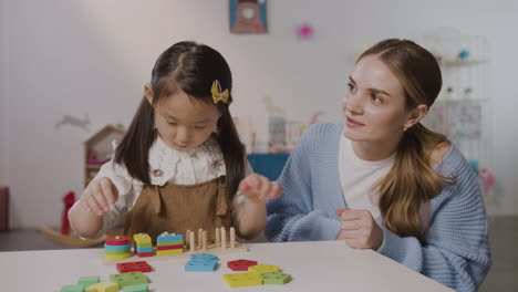 Little-Girl-In-A-Montessori-School-Playing-With-Shapes-Stacking-While-Teacher-Helping-Her-2