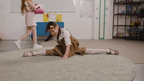 Kleines-Mädchen,-Das-Ihren-Körper-Streckt,-Während-Sie-Ihre-Beine-Auf-Dem-Teppich-Im-Klassenzimmer-In-Einer-Montessori-Schule-Spreizt