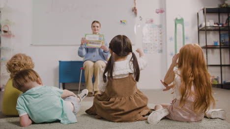 Female-Teacher-Teaching-Words-To-Her-Pupils-Whi-Are-Sitting-On-The-Floor-In-Classroom-In-A-Montessori-School