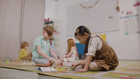 Kleines-Mädchen-Und-Kleiner-Junge-Spielen-Mit-Verschiedenen-Stücken-Auf-Dem-Teppich-Im-Klassenzimmer-In-Einer-Montessori-Schule